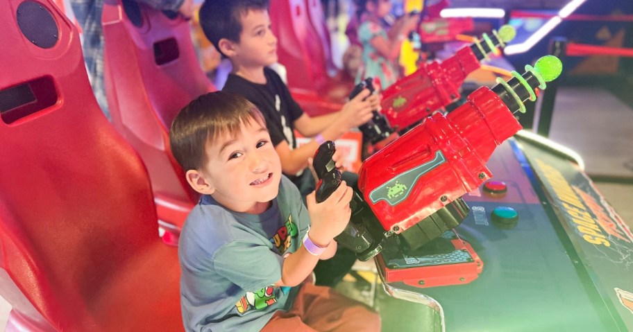 kids in an arcade ride sitting in red chairs with steering wheels playing a game