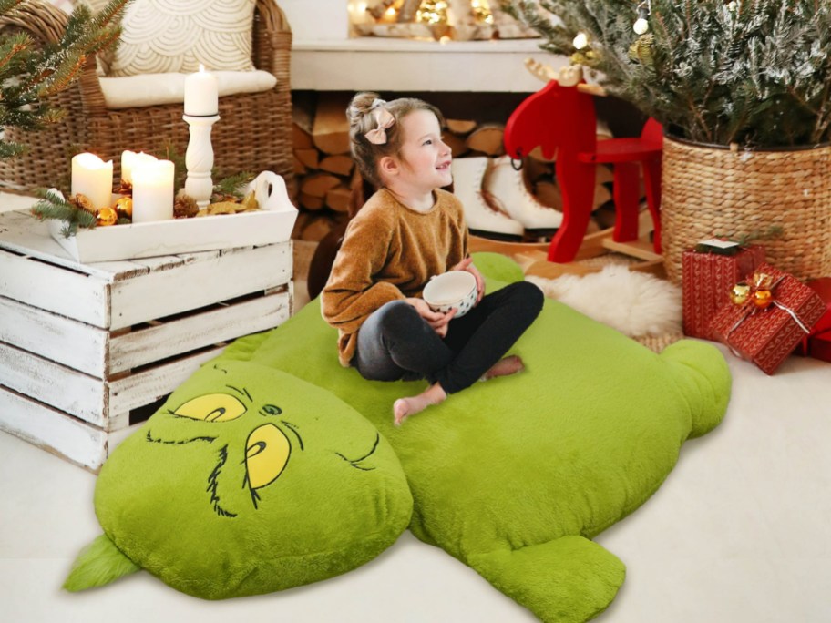 little girl holding a mug sitting on a grinch pillow