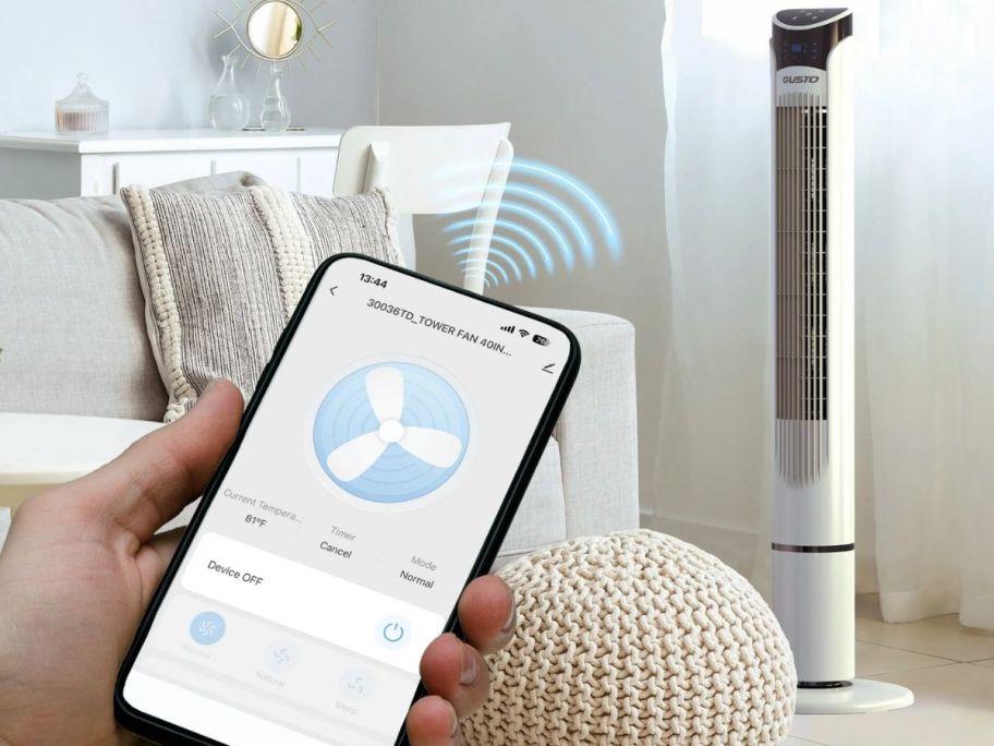 person holding phone with gusto smart app showing and tower fan in background