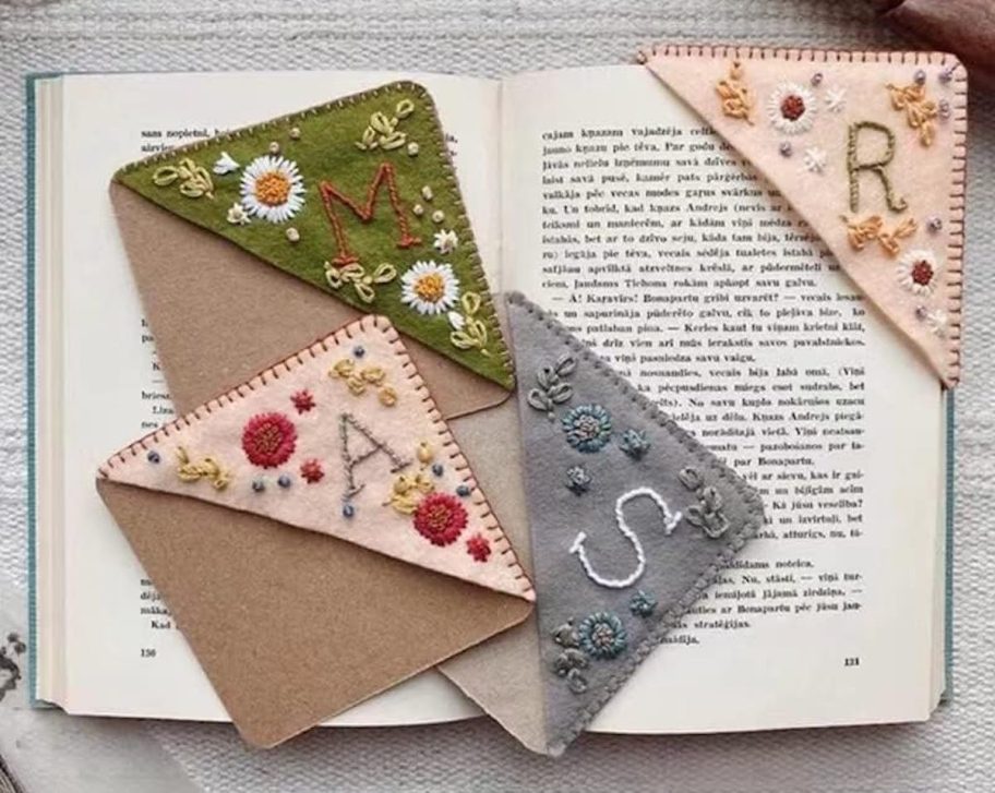 embroidered corner bookmarks with initials laying on top of open book