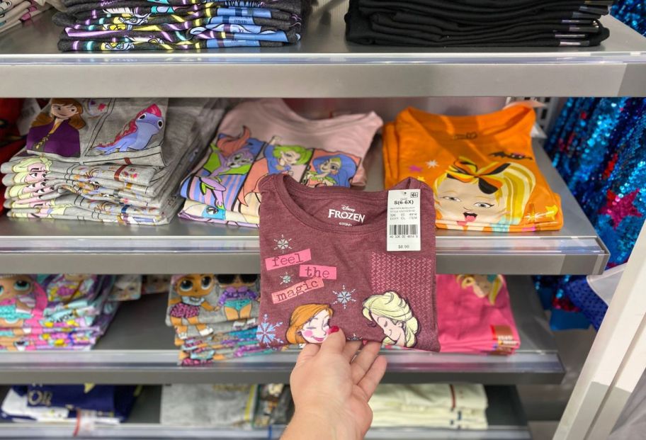 a womans hand grabbing a kids disney tee on a store shelf at a target store