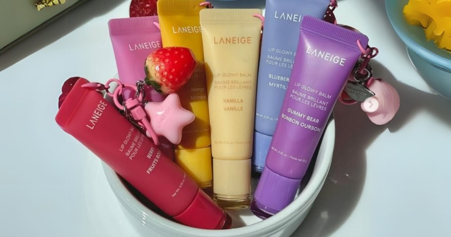 a white bowl with several different colors and flavors of Laneige Glowy Lip Balm tubes, some of them have charms added