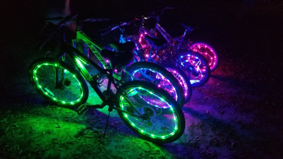 row of bikes in dark with different colored led lights on wheels