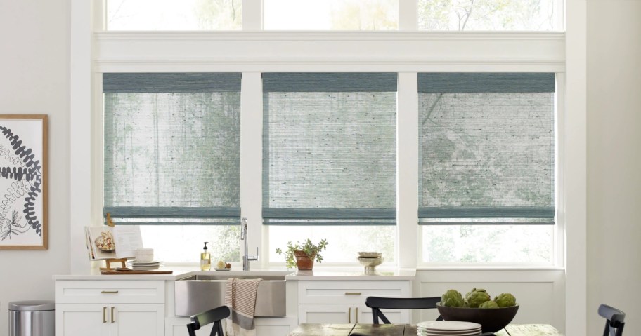 a kitchen sink and counter with 3 windows above it with green shades partly down