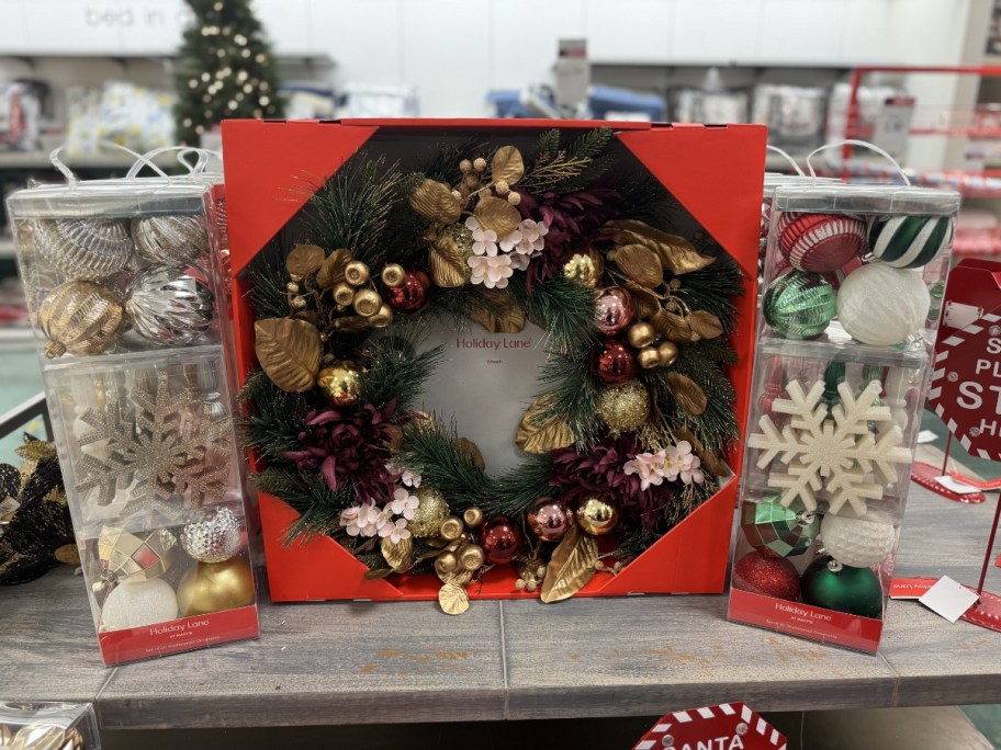 boxes of Christmas Ornaments and a box with a large Christmas Wreath on a store display table