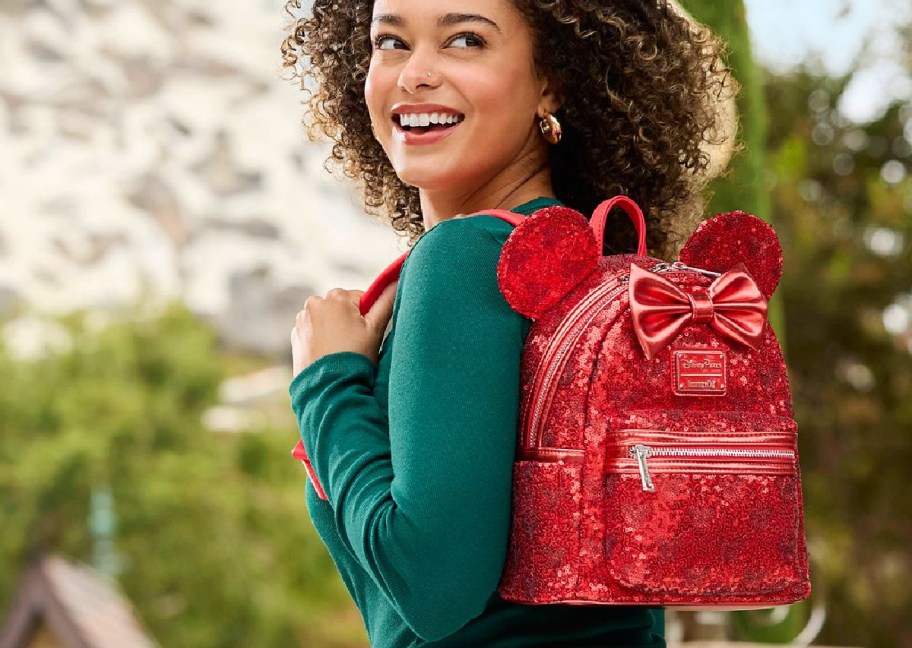 smiling woman wearing a minnie mouse red sequin loungefly mini backpack and matching minnie ears