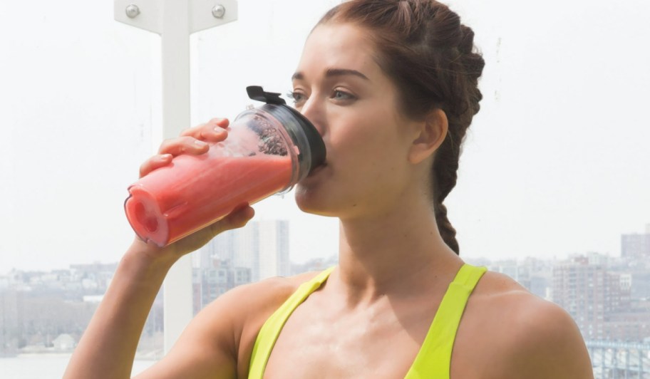 woman in bright green tank drinking a pink smoothie from a ninja blender cup