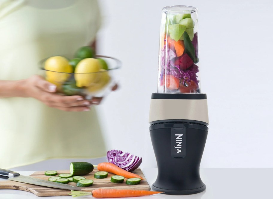 ninja fit personal blender on counter with woman holding clear bowl of citruses