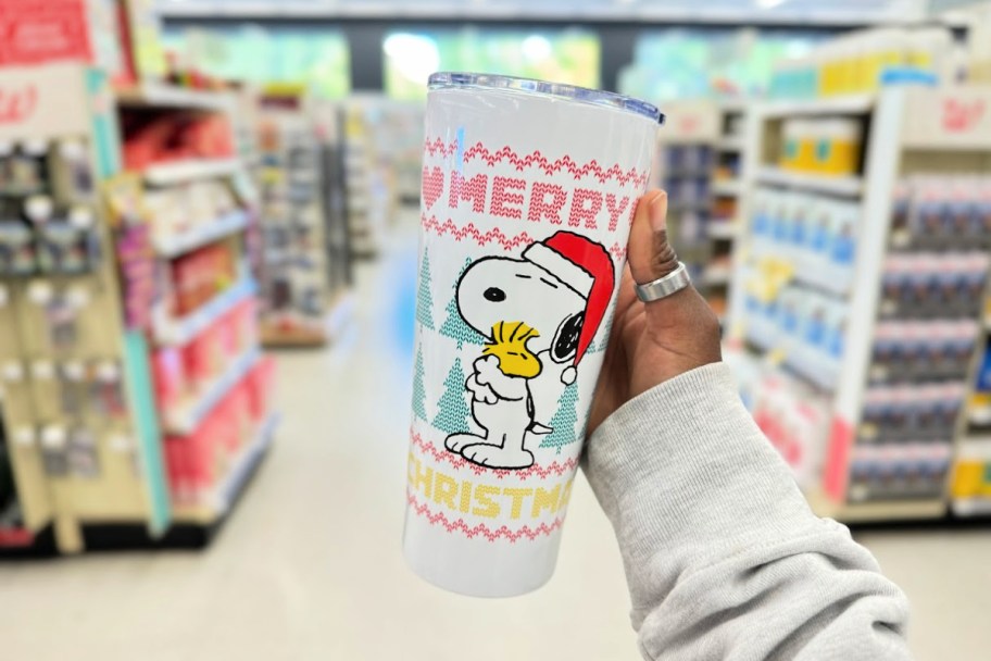 person holding a white holiday tumbler that has snoopy and woodstock depicted on the front