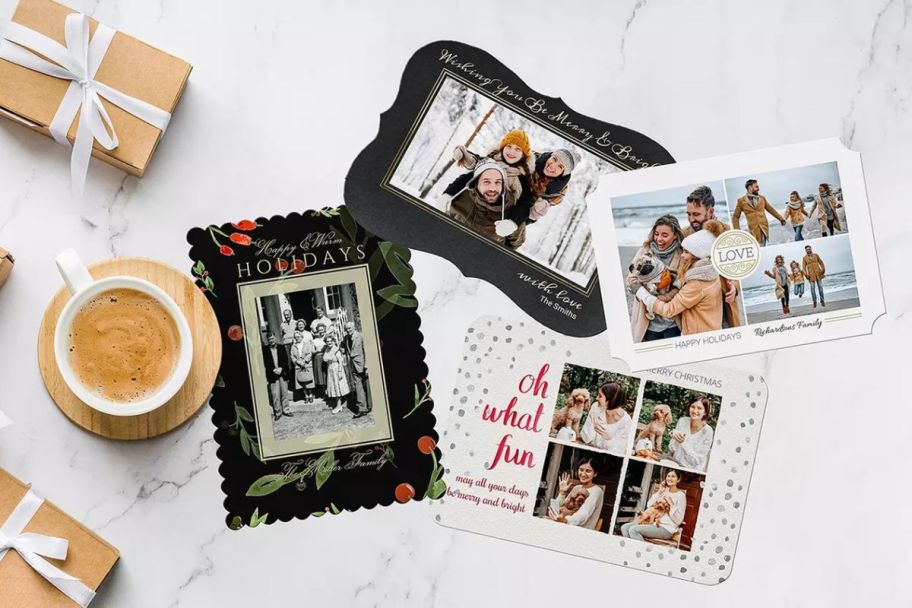 four assorted Holiday photo cards on a tabletop shown with a cup of hot cocoa