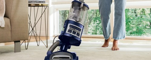 person pushing blue and gray shark vacuum on carpet