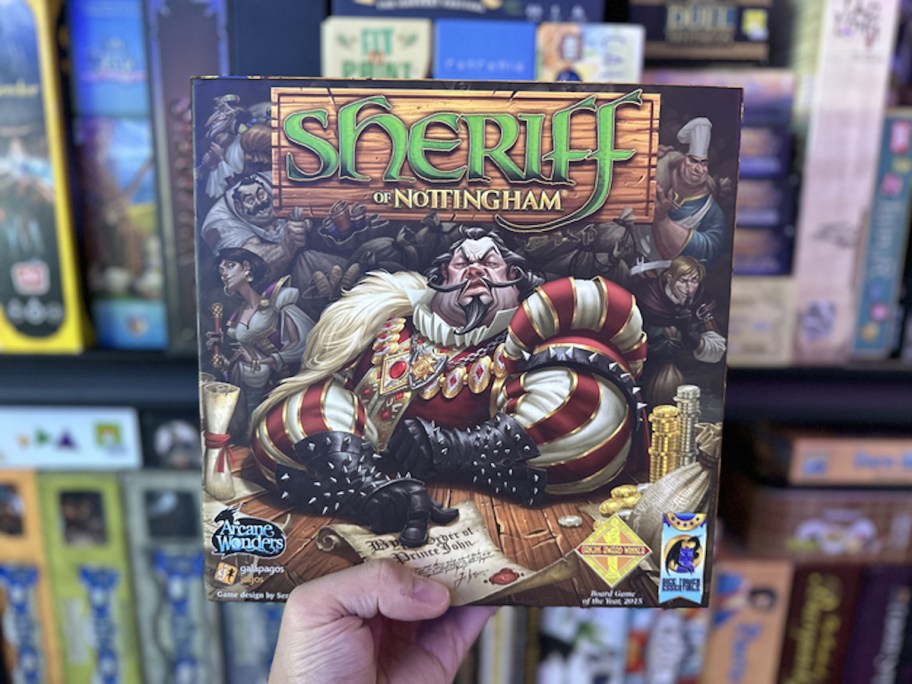 hand holding sheriff of nottingham board game in front of shelf