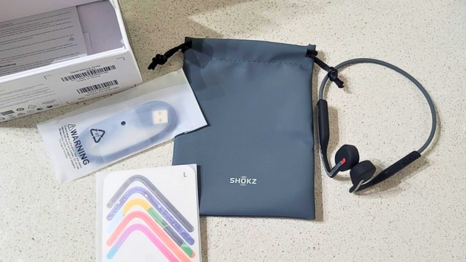 a pair of open ear headphones shown with storage bag charging cable and trim colors