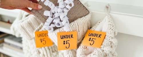 hand putting wrapped present into stocking with orange under $5 post it note