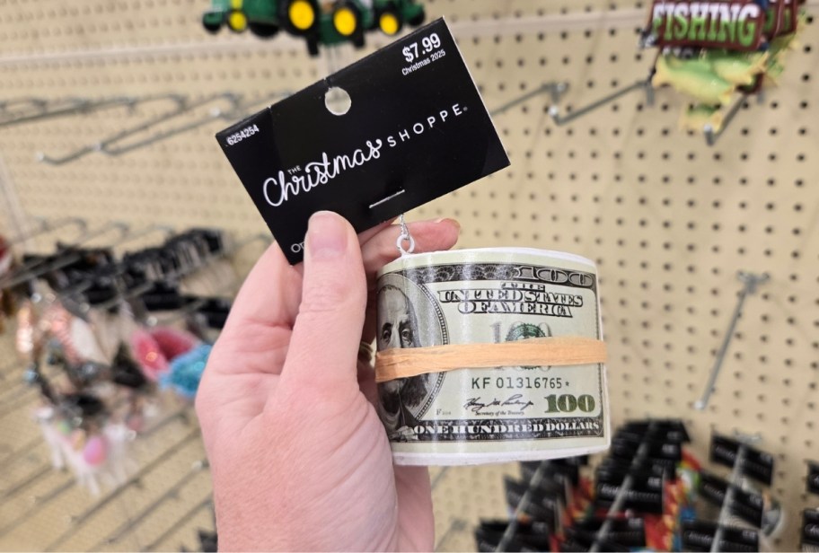 a womans hand holding a christmas ornament that looks like a roll of 100 bills