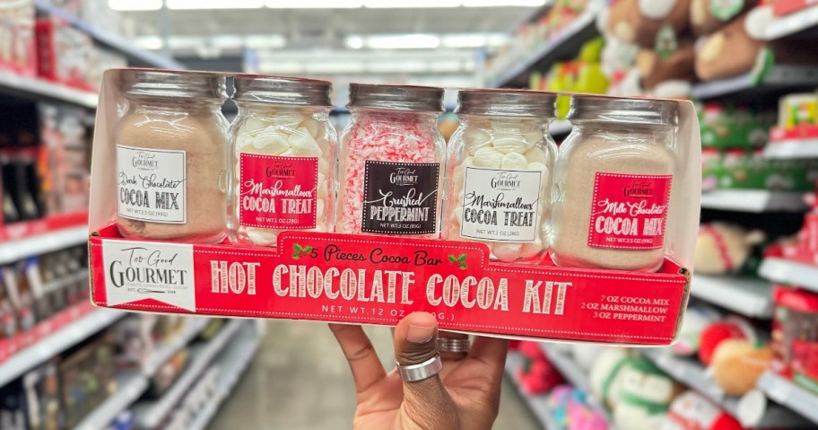 hand holding a box with 5 glass jars with various items to make hot cocoa, the box label says "Hot Chocolate Cocoa Kit"