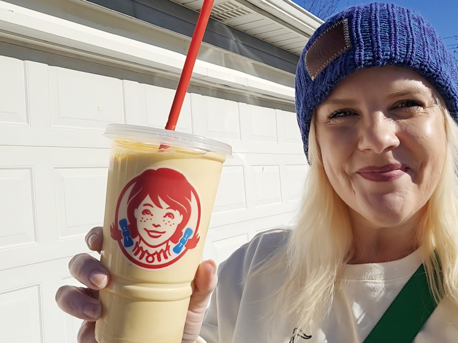 womanin a navy blue beanie smiling and holding a wendy's caramel frosty