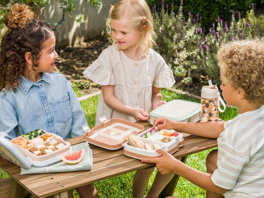 Three kids eating bentogo lunchbox at picnic table