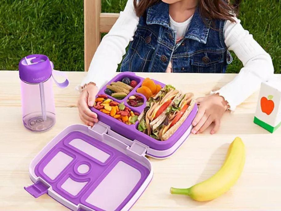 Girl eating lunch from a bent child's lunch box with a bent bottle of water next to her