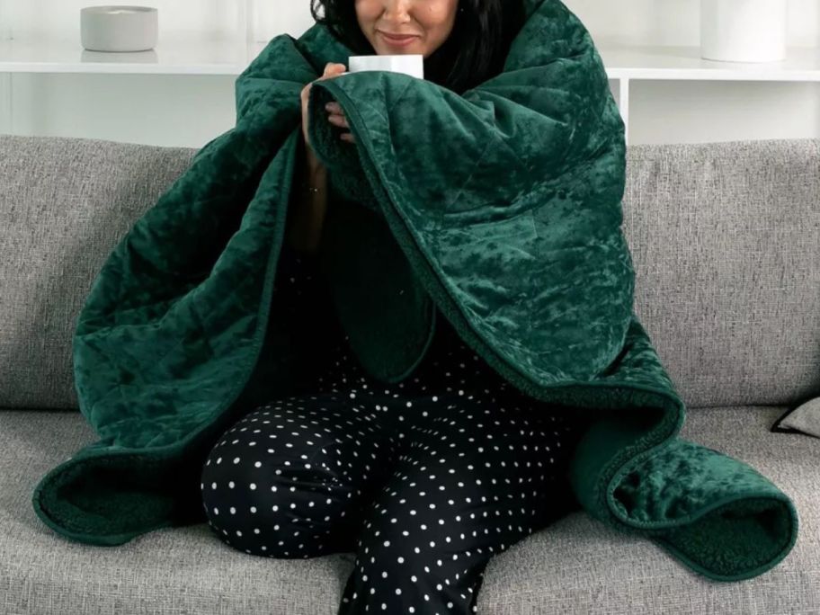 woman drinking from a mug on a couch with a Brookstone heated throw wrapped around her