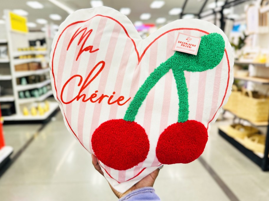 hand holding up a heart shaped pillow with cherries