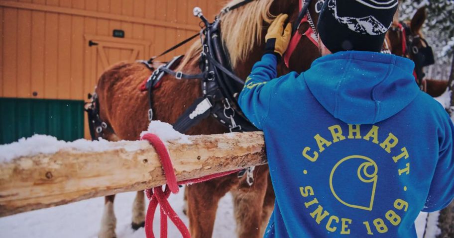 man wearing a Carhartt sweatshirt petting a horse 