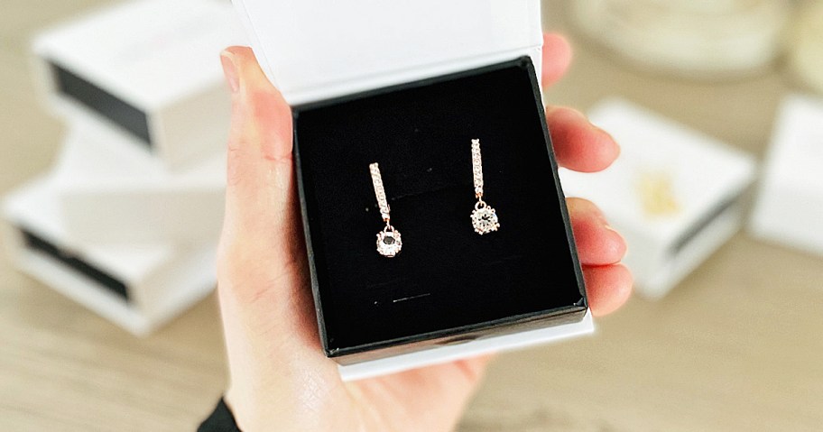 hand holding a pair of drop earrings in a jewelry box