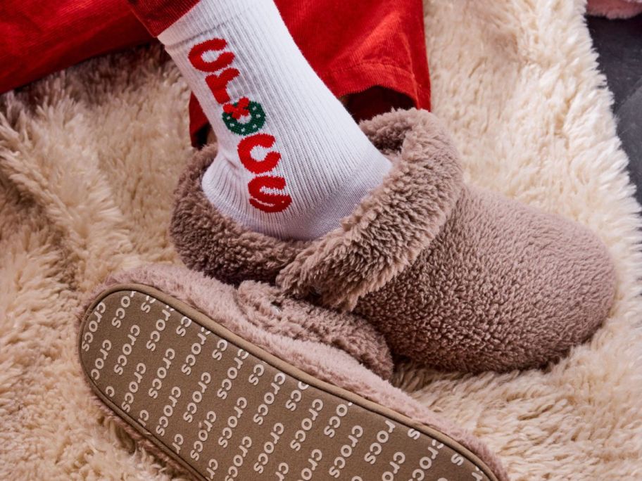 A person wearing Crocs Adult Classic Cozy Slippers on a fluffy rug.
