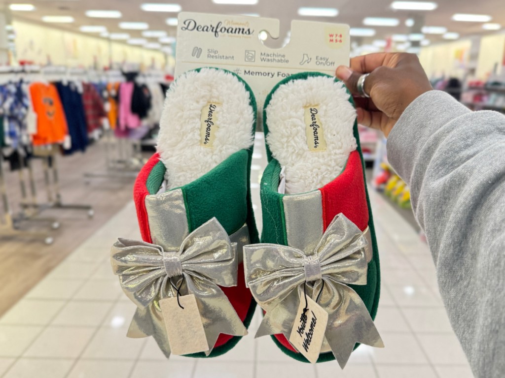 woman holding up dearfoams holiday ribbon slippers in store