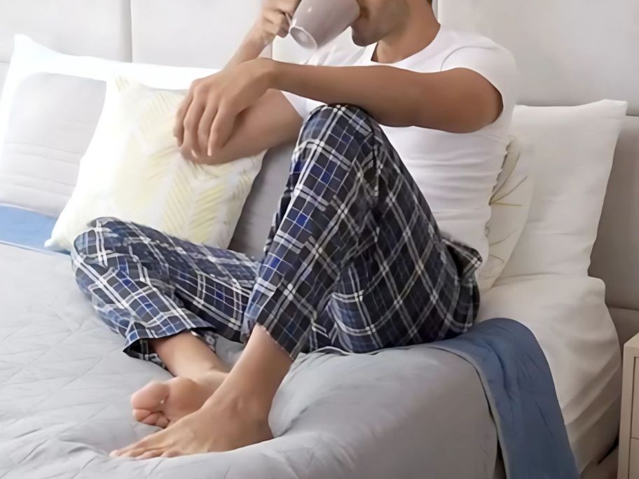 A man having a cup of coffee on a bed wearing Fruit of the Loom Pajamas