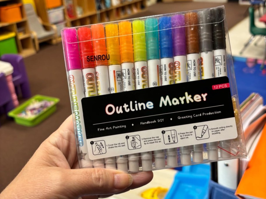 A hand holdin up a box of glitter outline markers.