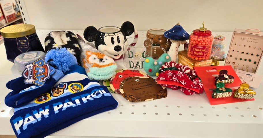 various items on a store shelf - kids beanie, women's fuzzy socks, a holiday jar candle, a Mickey Mouse coffee mug, Christmas ornaments, a pack of earrings, Christmas hair accessories, Sephora Face Masks and more.