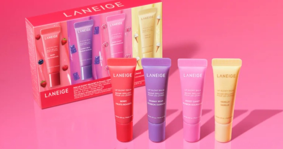 a 4 piece set of Laneige glowy lip balms in dark pink, purple, yellow, and light pink colors next to the box it comes in, on a pink background