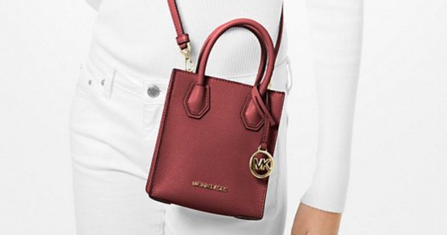 woman in a white top and white jeans wearing a dark reddish color crossbody bag