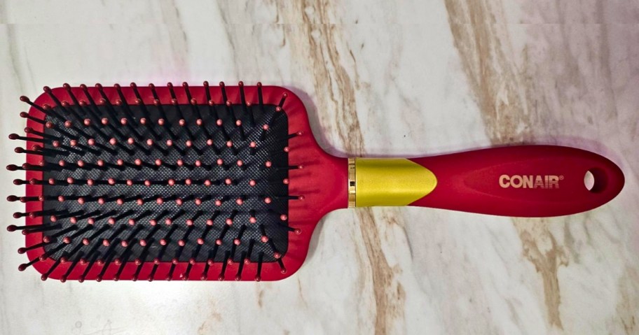 a Conair velvet touch rectangle wide hair brush in a red color laying on a marble countertop