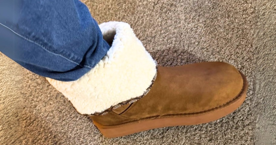 a women's lower leg and foot wearing blue jeans and a tan platform suede boot with a shearling foldover around the ankle