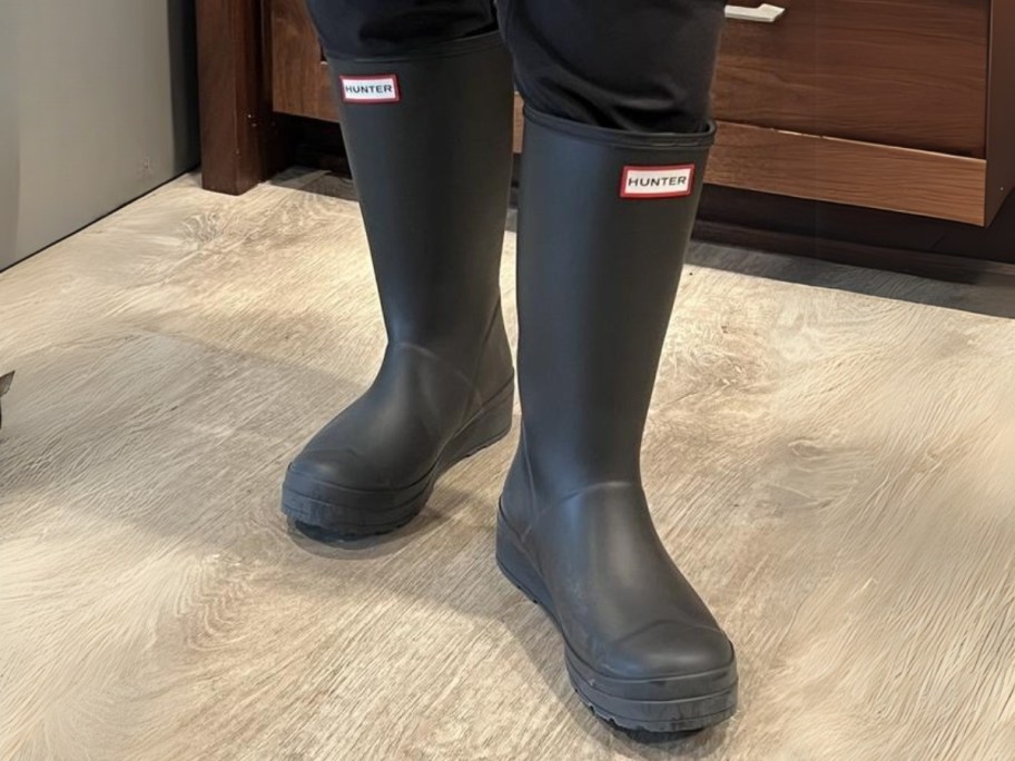 women's legs and feet wearing black rubber Hunter brand rain boots that hit mid calf