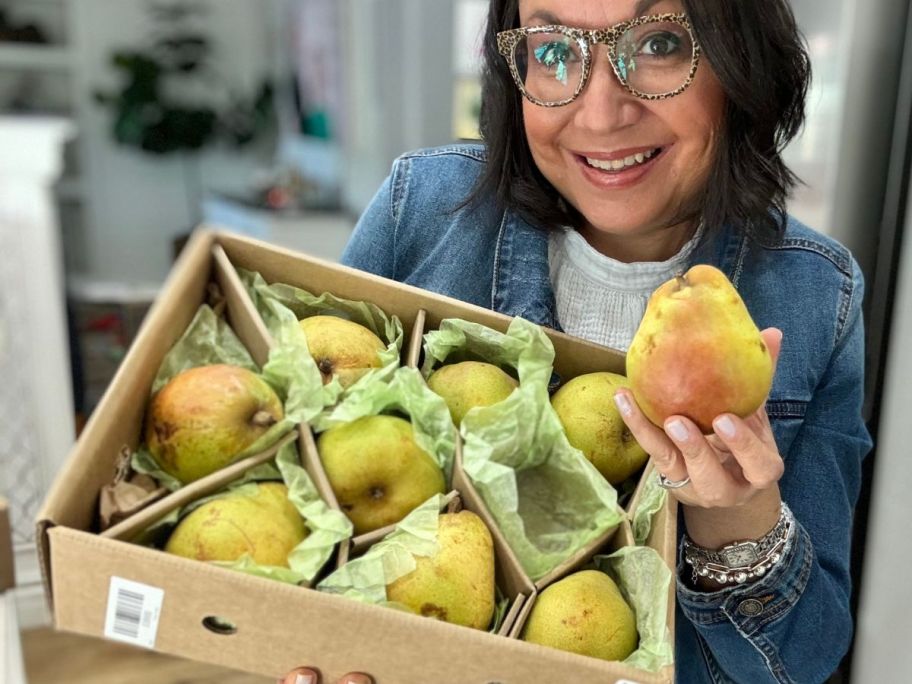 Woman holding up a Harry & David Maverick Pear next to a whole box of pears