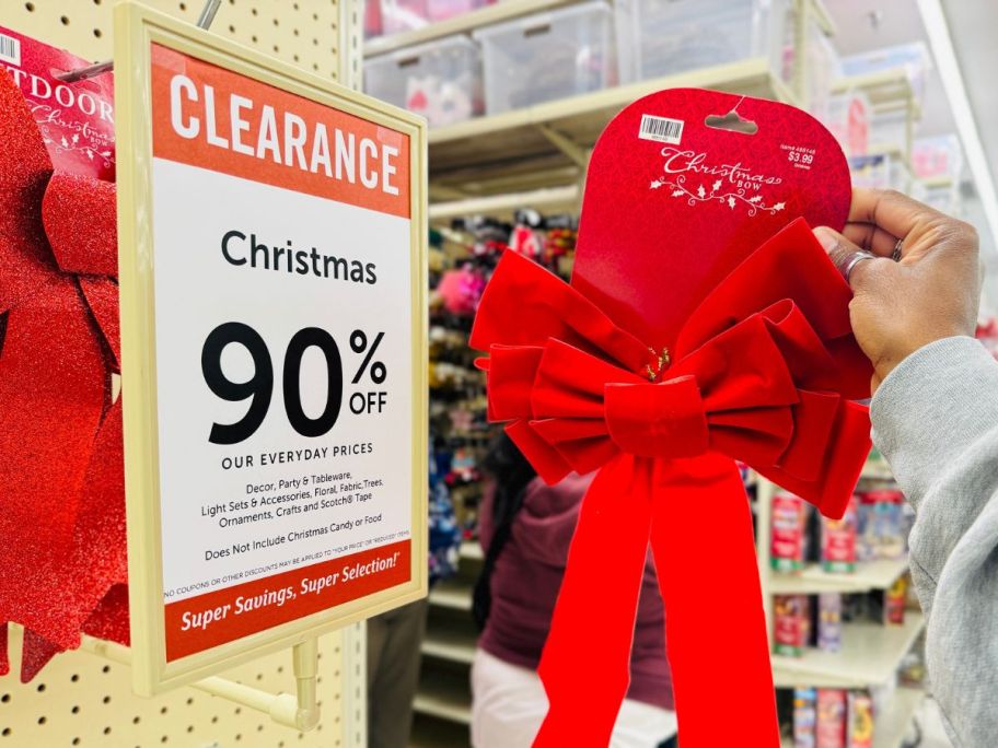 Hand holding a red holiday bow next to a 90% off sign at HObby Lobby