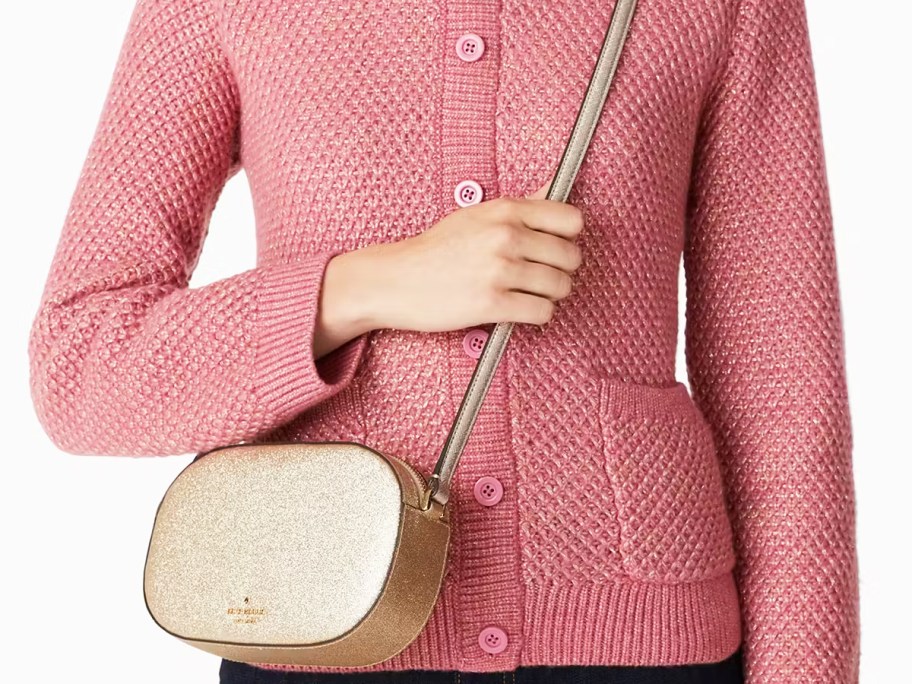 woman in a pink sweater with a glittery gold oval crossbody bag