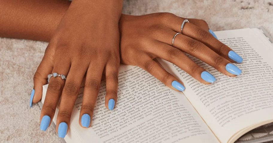 Women's hands wearing blue press on nails with hands crossed resting on a book