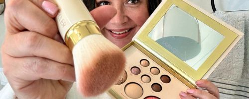 Woman holding a laura Geller makeup kit and kabuki brush