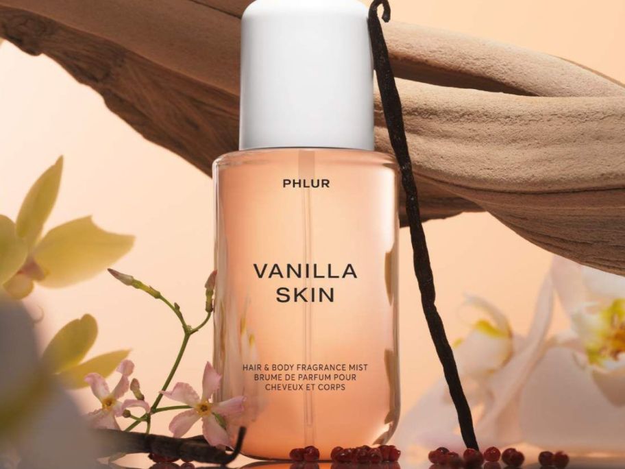 Phlur Vanilla Skin Spray next to a vanilla bean and flowers