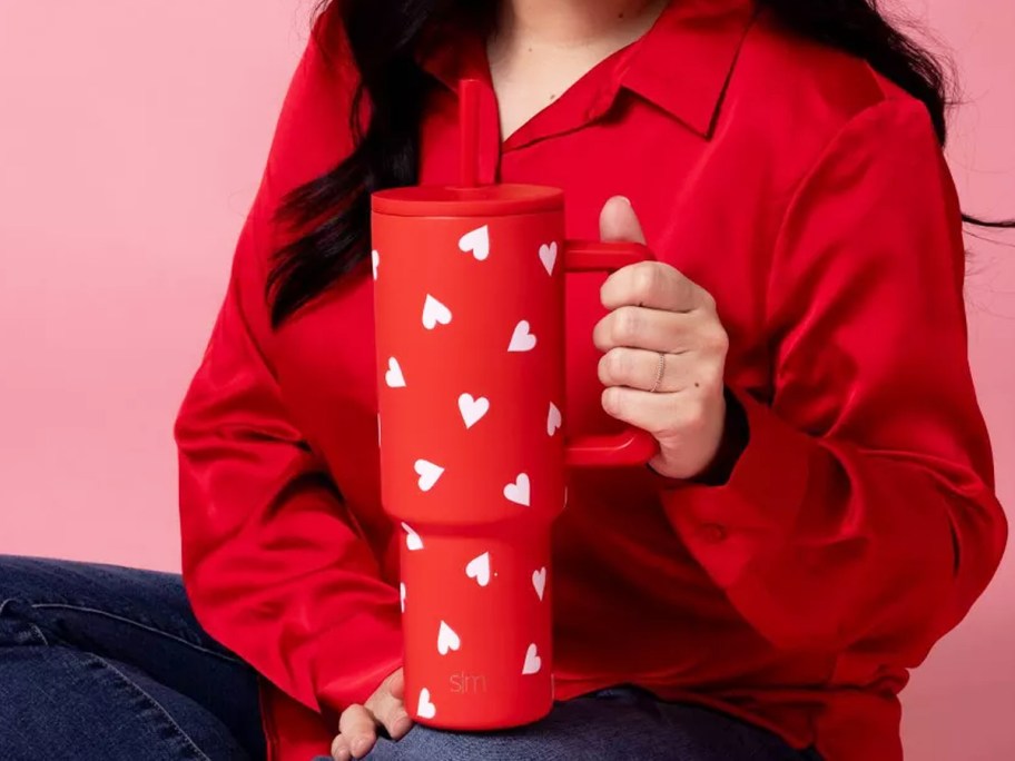 woman holding up a red tumbler with white heart print