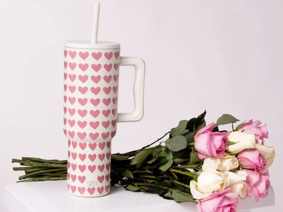 white tumbler with pink heart print next to bouquet of roses