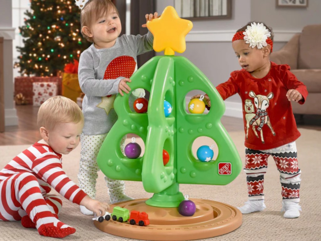 Three small kids playing with plastic green step to my first Christmas tree