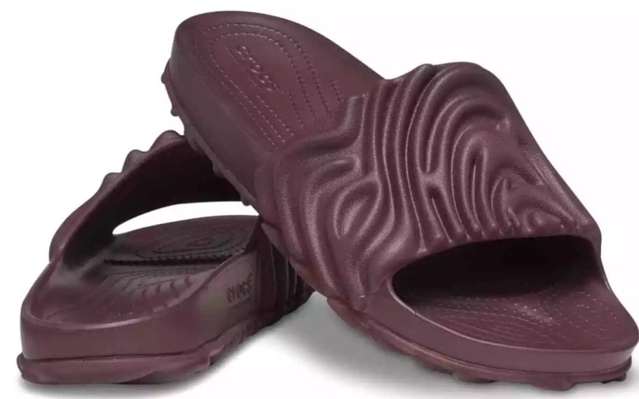 a pair of Crocs slides shoes in a dark purple brown color, the pattern is a wavy style