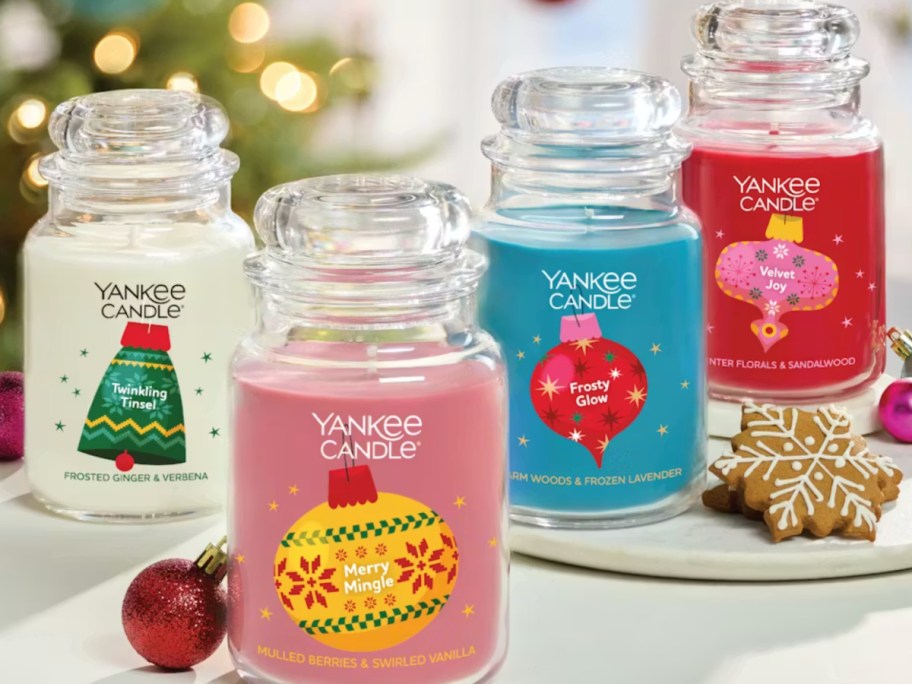 Four different Christmas themed Yankee candles on display in front of lighted tree
