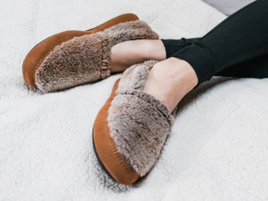 a woman's feet and legs wearing black leggings and greyish tan slippers