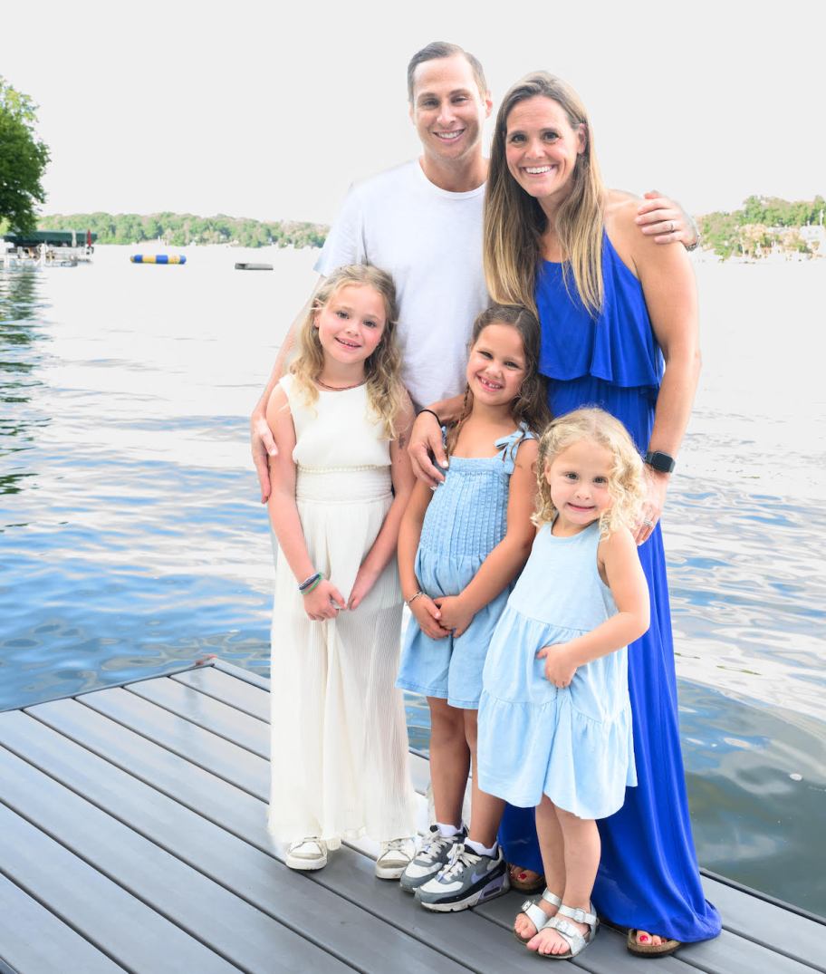 family with three young girls smiling standing on dock on water